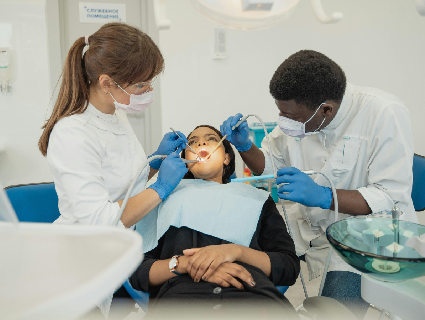 mulher deitada em uma cadeira odontológica, enquanto dentista e auxiliar bucal fazem procedimento