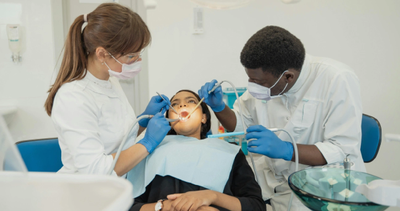 mulher deitada em uma cadeira odontológica, enquanto dentista e auxiliar bucal fazem procedimento